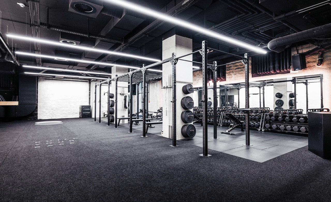 Dunkles, modernes Fitnessstudio mit schwarzem Boden, Hanteln und Trainingsracks.