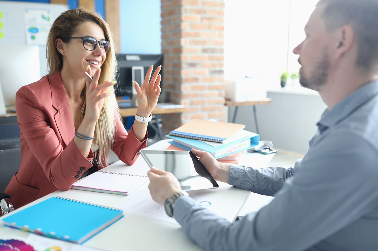 Die qualitative Fachkraft wird zum primären Wirtschaftsfaktor. Um im Wettbewerb dauerhaft zu bestehen, muss die Personalbeschaffung professionalisiert und systematisiert werden Frau erklärt einem Mann lächelnd etwas i deiner Gesprächssituation an einem Schreibtisch