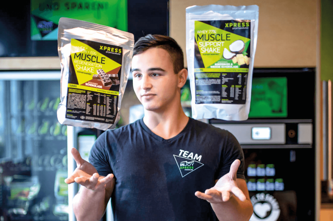 Ein Fitnessstudiomitarbeiter wirft zwei Packungen Proteinpulver in die Luft.
