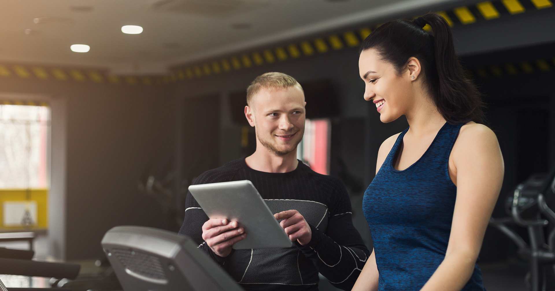 Trainer geht mit Mitglied Trainingsplan im Fitnessstudio durch