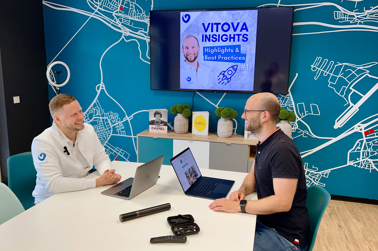 Zwei Mitarbeiter der Vitova-Gruppe sitzen an einem Tisch mit ihren Laptops und sind im Gespräch.