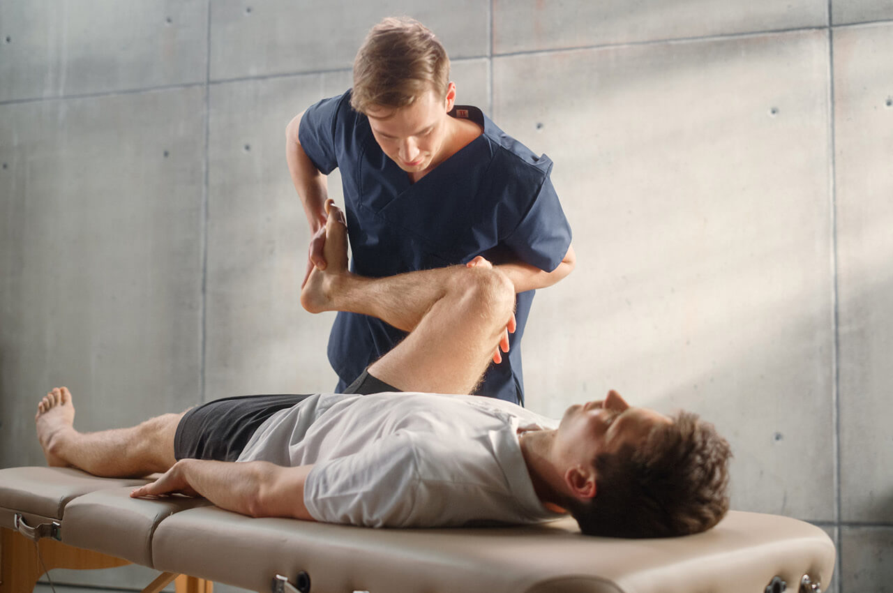 Abwechslungsreiche Tätigkeiten spielen heute eine zentrale Rolle. Mitarbeiter, die täglich ausschließlich an der Bank arbeiten, verlieren langfristig oft Motivation und Energie Physiotherapeut behandelt Knie von einem Patienten auf einer Liege