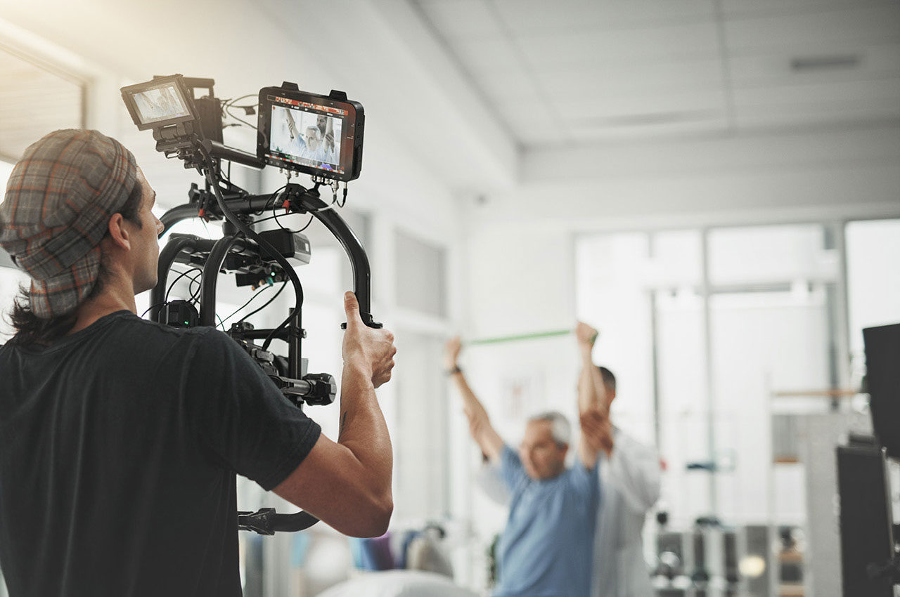 Ein Videograf filmt einen Physiotherapeuten bei seiner Arbeit mit einem Patienten.