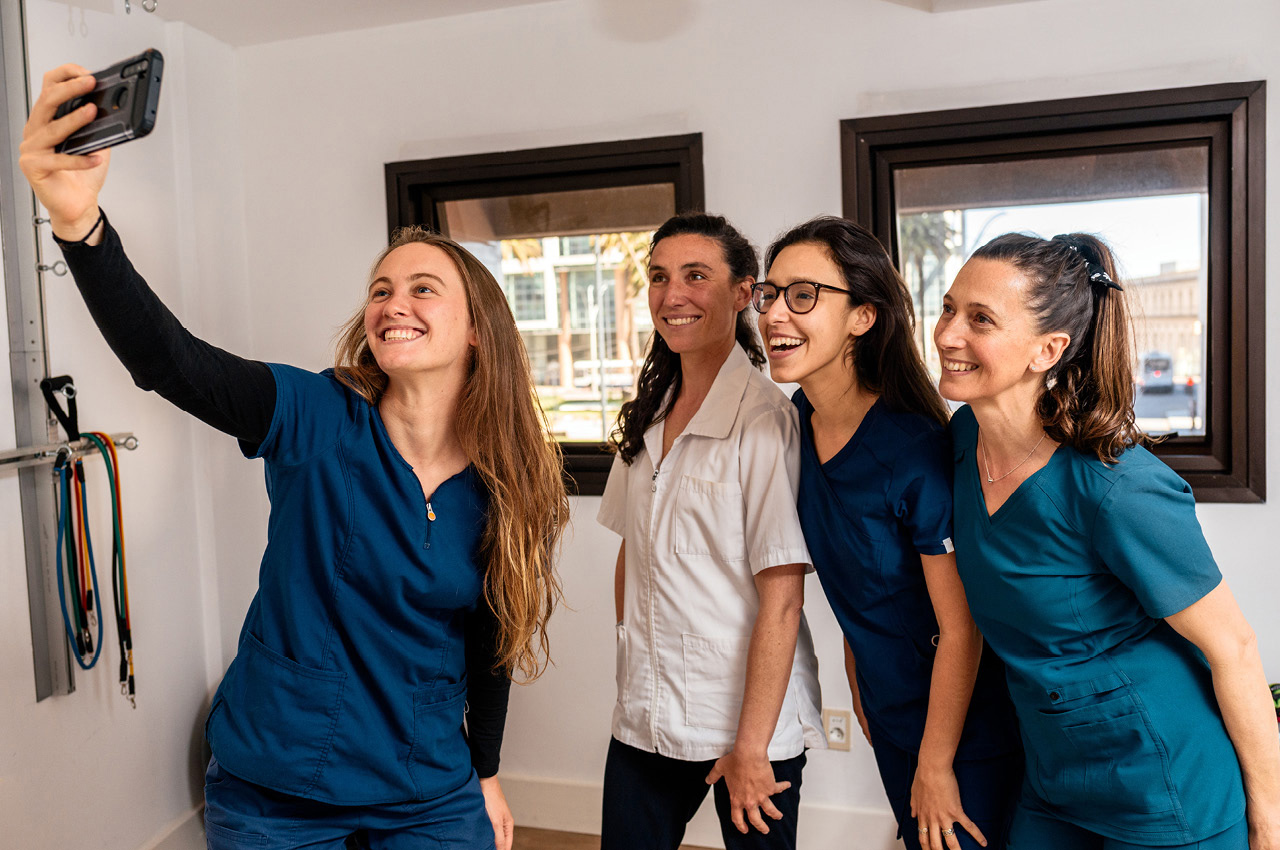 Vier Physiotherapeuten blicken lächeln in ein Smartphone und nehmen ein Selfie auf.