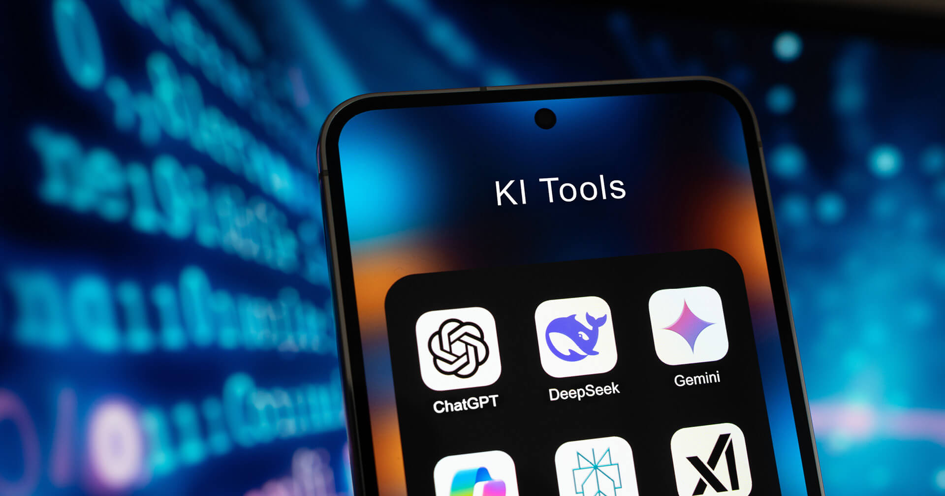 Nahaufnahme eines Smartphones, das den Ordner "KI Tools" anzeigt. Sichtbar sind die App-Icons und Namen von drei Künstlicher-Intelligenz-Anwendungen: ChatGPT, DeepSeek und Gemini. Der Hintergrund ist unscharf und zeigt blau leuchtende, codegleiche Zeichen auf einem Bildschirm, was die digitale oder technische Natur der Anwendungen unterstreicht.