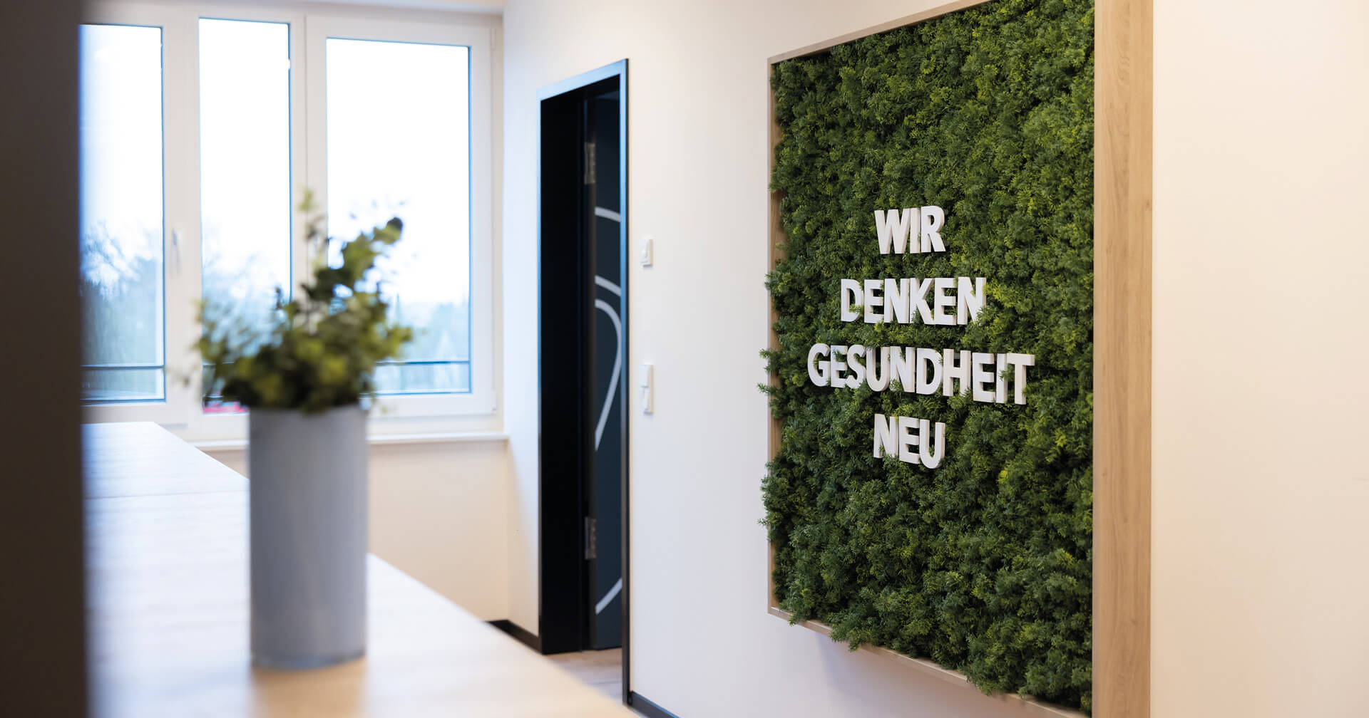 Praxiseingang mit Pflanzen und Schriftzug an der Wand