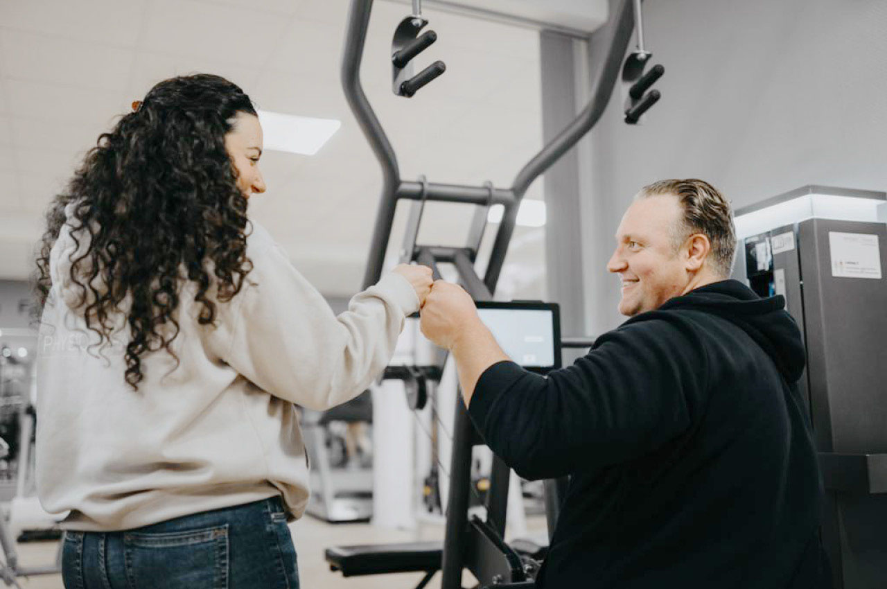 Mann trainiert im Fitnessstudio und gibt der Trainerin einen Fistbump