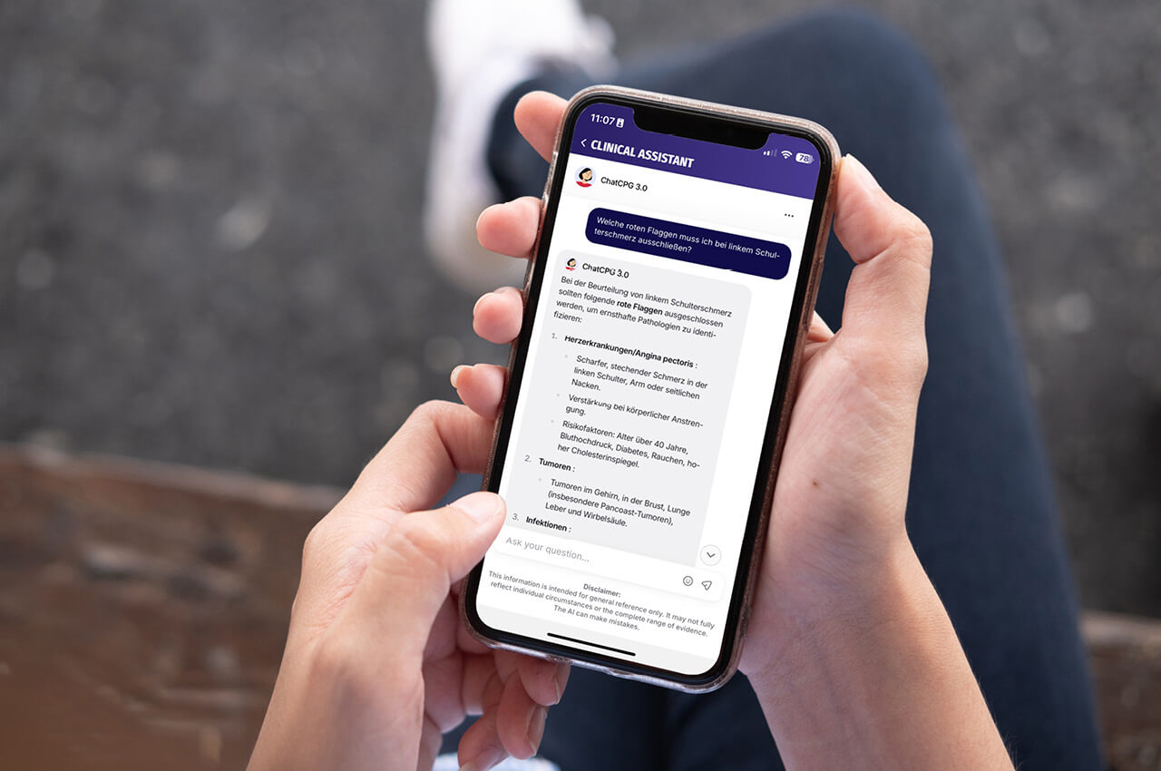 Eine Nahaufnahme zeigt zwei Hände, die ein Smartphone halten, auf dessen Display die App "CLINICAL ASSISTANT" geöffnet ist. Die App zeigt eine KI-generierte Antwort auf die Frage: "Welche roten Flaggen muss ich bei linkem Schulterschmerz ausschließen?". Die Antwort listet drei potenzielle, ernste Erkrankungen auf und deren Ausschlusskriterien. Im Hintergrund sind unscharf die Beine einer Person in dunkler Hose und weißen Schuhen zu sehen.