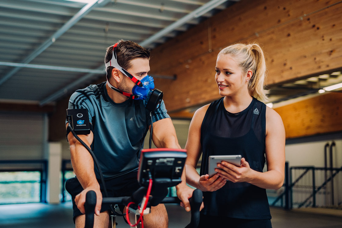 Fitnessstudiomitglied und Trainerin machen eine Atemgasanalyse mit einem Gerät von Dynostics